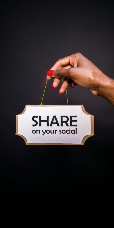 A hand holds a sign reading 'Share on your social' against a dark background.
