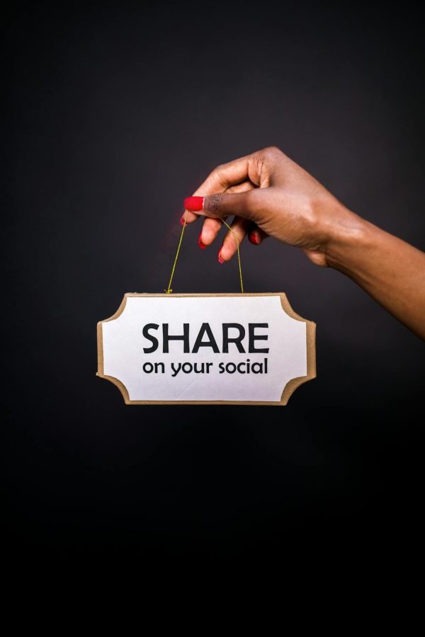 A hand holds a sign reading 'Share on your social' against a dark background.