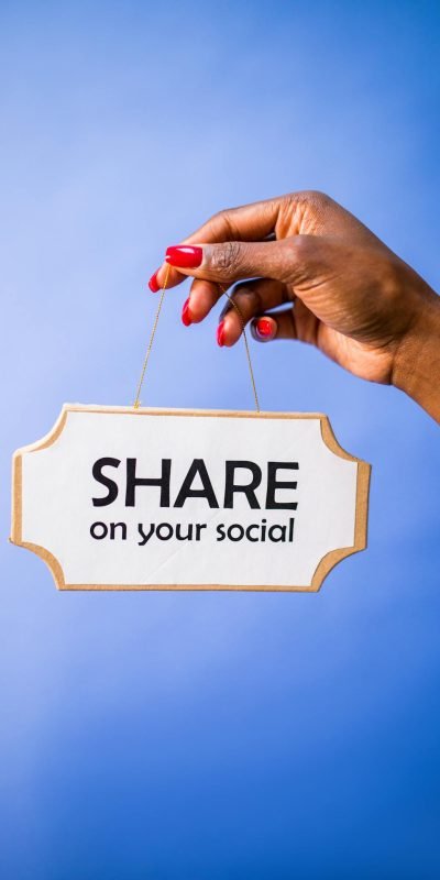 Close-up of a hand holding a 'Share on your social' sign on a vibrant blue backdrop.