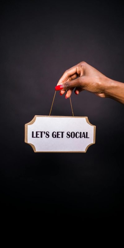 Close-up of a hand holding a sign with 'Let's Get Social' on a dark background.