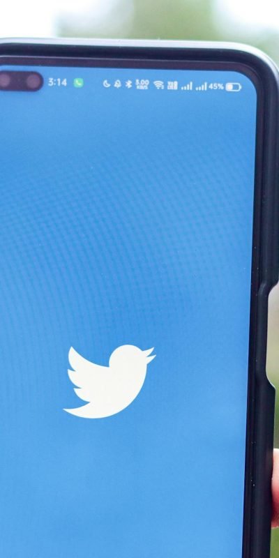 Hand holding smartphone with Twitter app open against blurred natural background.